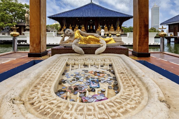 Reclining Buddha statue in a temple with coins in the foreground, The Seema Malaka Temple with the Buddha statues in Colombo Sri Lanka