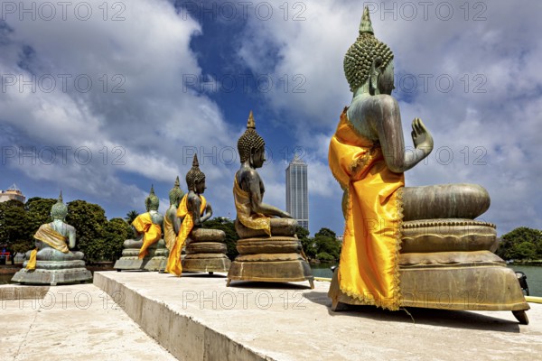 Buddha statues on the water with yellow robes against an urban backdrop, The Seema Malaka Temple with the Buddha statues in Colombo Sri Lanka