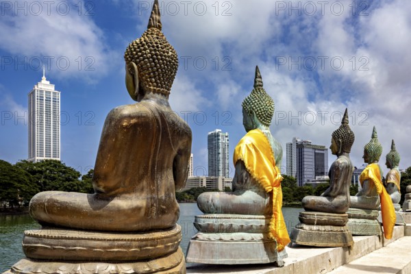 Back views of Buddha statues with yellow fabrics in front of a modern city, The Seema Malaka Temple with the Buddha Statues in Colombo Sri Lanka