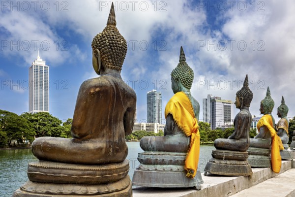 Buddha statues in bronze with yellow cloths in front of skyscrapers and water, The Seema Malaka Temple with the Buddha statues in Colombo Sri Lanka