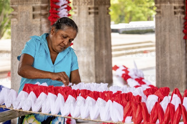 Woman making red and white decorations in an enclosed space, people making garlands in Colombo Sri Lanka City Hall