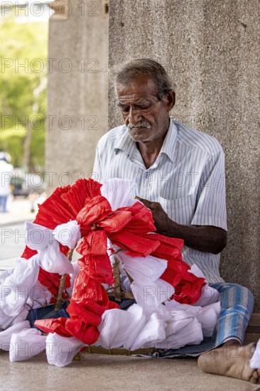 Elderly man sitting and concentrating making flowers, people making garlands in Colombo Sri Lanka City Hall