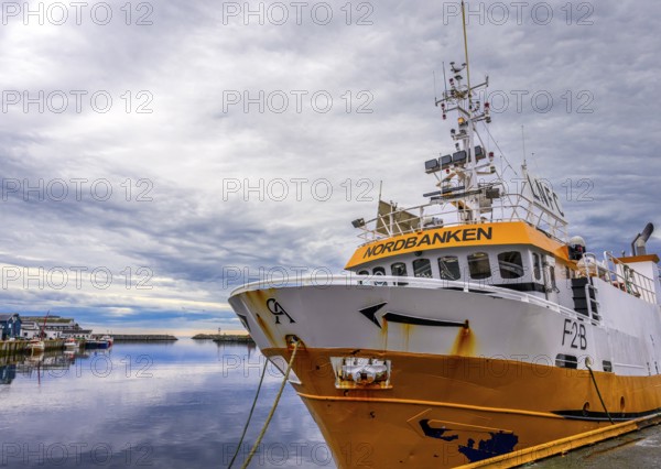Yellow and white ship in quiet harbor with cloudy sky in the background, Berlevag, Finnmark, Nirwegen