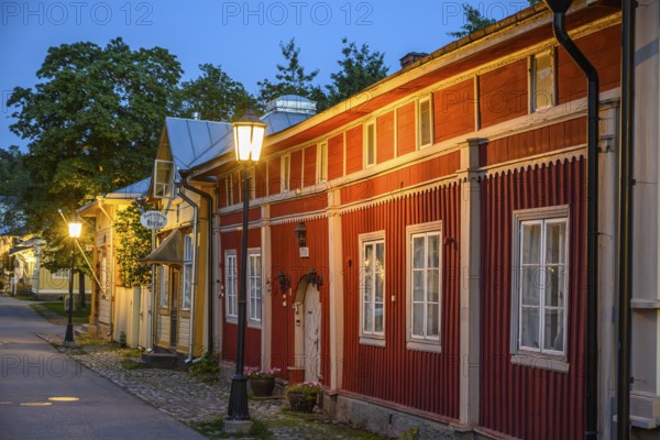 Street scene in the old town of Naantali, red historic wooden building with decorative windows on a paved street in the evening light with cozy street lighting, Naanatali, Varsinais-Suomi, Finland