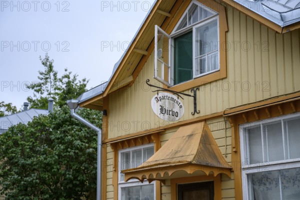 Street scene in the old town of Naantali, yellow wooden house with a rustic charm and a sign surrounded by trees