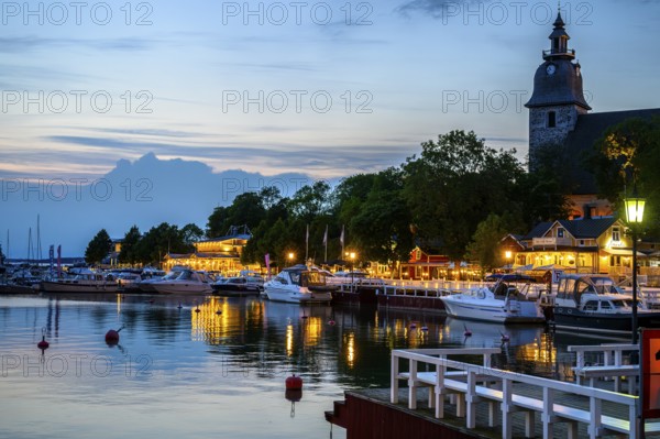 Street scene in the old town of Naantali, evening mood at the harbor with illuminated buildings and the church and boats on the water, Naanatali, Varsinais-Suomi, Finland