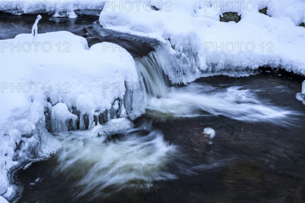 Ilsenburg, Saxony-Anhalt, Germany, Small waterfall of the river Ilse in the Harz National Park on the Heinrich Heine trail Ilsetal hiking trail with ice-covered banks and running water