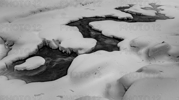 Ilsenburg, Saxony-Anhalt, Germany, A frozen one on the Ilse river in the Harz National Park on the Heinrich-Heine trail Ilsetal hiking trail in a snowy black and white winter landscape