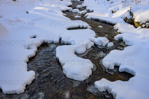 Ilsenburg, Saxony-Anhalt, Germany, A stream flows through a snow-covered landscape with layers of ice on the Ilse river in the Harz National Park on the Heinrich-Heine trail Ilsetal hiking trail