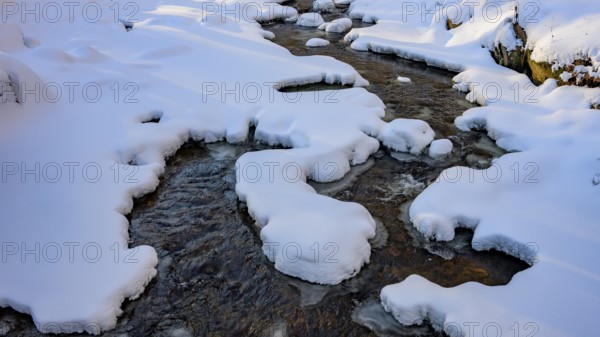 Ilsenburg, Saxony-Anhalt, Germany, snowy Ilse river in the Harz National Park on the Heinrich-Heine trail Ilsetal hiking trail, illuminated by light and shadow in winter