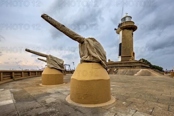 A lighthouse next to two cannons on a paved area under a cloudy sky, The Colombo Sri Lanka lighthouse