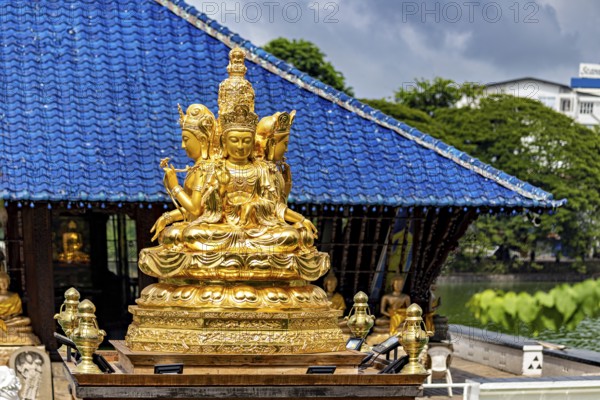 Golden Buddhist statue in front of a blue roof with cloudy sky, The Seema Malaka Temple with the Buddha Statues in Colombo Sri Lanka
