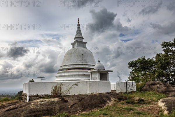 White stupa against dramatic sky surrounded by natural terrain, tranquil atmosphere, The Maligatenna Purana Rajamaha Viharaya monastery near Colombo Sri Lanka