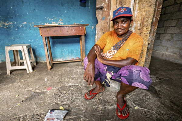 Smiling man wearing cap squats relaxed in a simple room, people in the streets of Slave Island in Colombo Sri Lanka