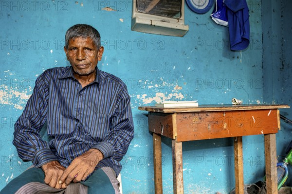 Man sitting relaxed in front of a blue wall in a simple room, people in the streets of Slave Island in Colombo Sri Lanka
