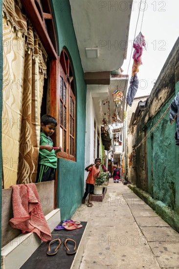 Children look out of windows in a narrow, colorful alley, people in the streets of Slave Island in Colombo Sri Lanka