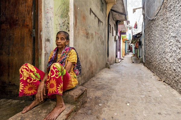 Elderly woman sitting pensively in a narrow alley, people in the streets of Slave Island in Colombo Sri Lanka