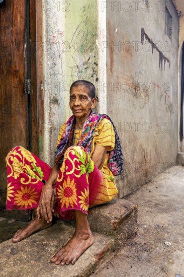Woman in colorful clothes sitting on a step in a narrow street, people in the streets of Slave Island in Colombo Sri Lanka