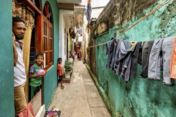 Children look out of a window, laundry hangs in a narrow alley, people in the streets of Slave Island in Colombo Sri Lanka