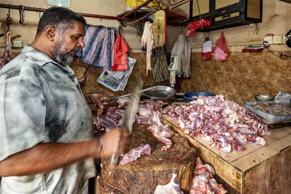 A butcher shreds pieces of meat with a cleaver on a wooden table in a traditional market atmosphere, butcher shop on the streets of Slave Island in Colombo Sri Lanka