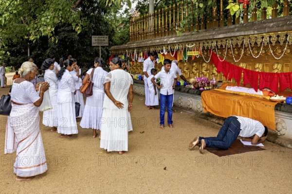 People in white celebrate a ceremony with prayers and offerings in front of a decorated altar, The Kelaniya Temple in Colombo Sri Lanka