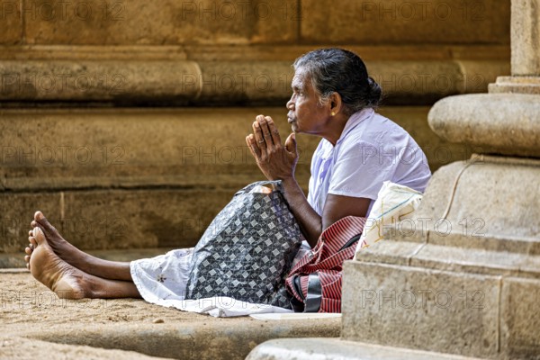 A woman sits in front of a stone temple and prays, surrounded by peace and traditional atmosphere, praying people at Kelaniya Temple in Colombo Sri Lanka