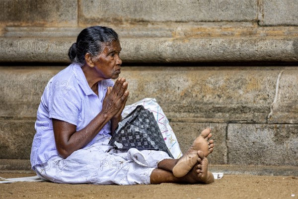 Elderly woman in humble position praying in front of a stone temple, with peaceful expression, praying people at Kelaniya Temple in Colombo Sri Lanka