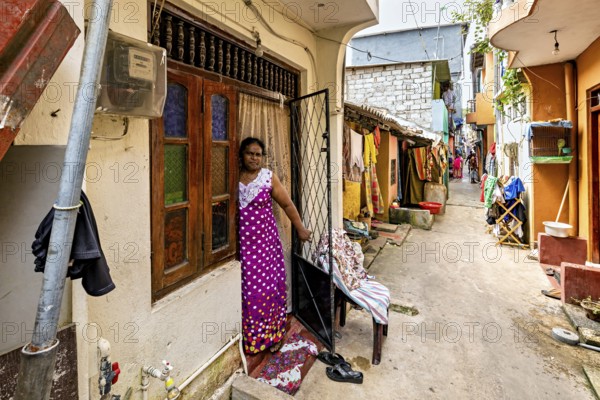 Woman in traditional dress standing in front of a house in the alley, people in the streets of Slave Island in Colombo Sri Lanka