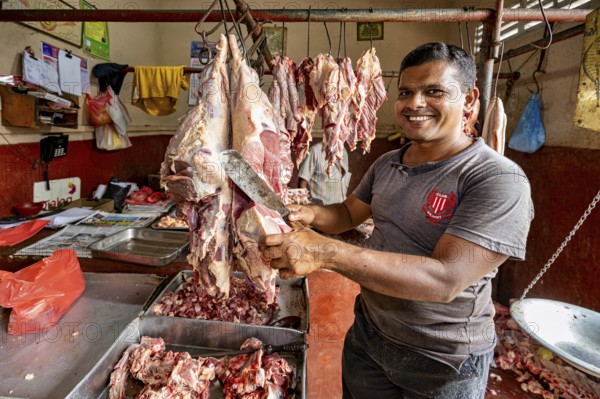 A smiling butcher cuts meat in a traditional shop, with pieces of meat around him, butcher shop in the streets of Slave Island in Colombo Sri Lanka