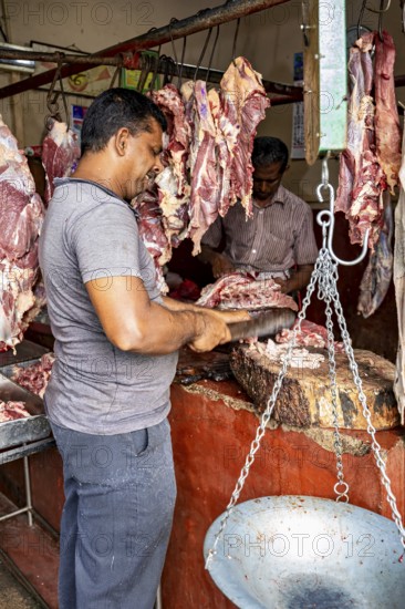 A butcher cuts meat at a market stall, pieces of meat hang in the background, traditional environment, butcher shop in the streets of Slave Island in Colombo Sri Lanka