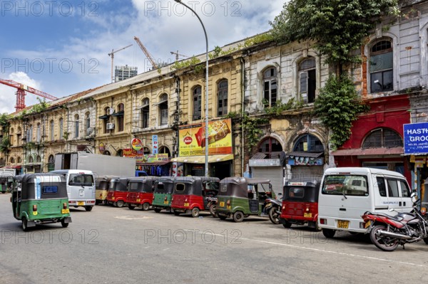 Busy urban street with old buildings and a series of tuk-tuks including a cloudy sky, tuk tuk in the streets of Colombo Sri Lanka