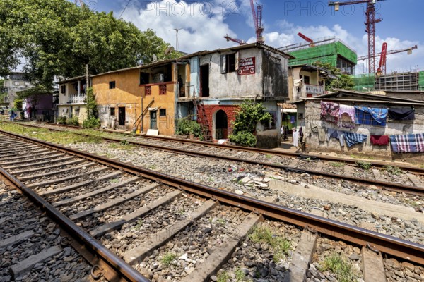 Construction cranes rise behind brightly painted houses along the train tracks under a blue sky, railway line in the historic Slave Island district in Colombo Sri Lanka