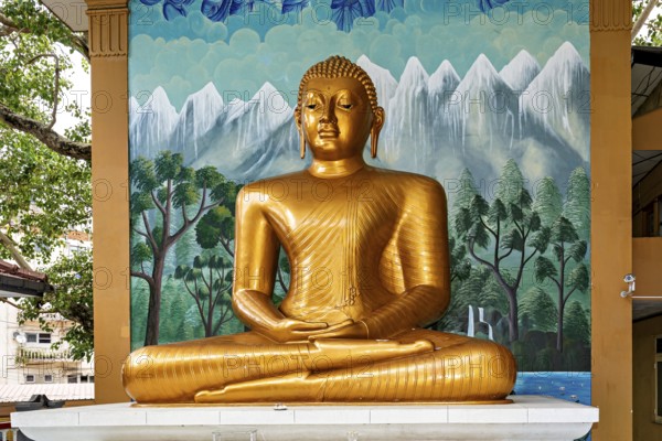Golden Buddha statue in front of a painted wall with landscape motif, The Seema Malaka temple with the Buddha statues in Colombo Sri Lanka