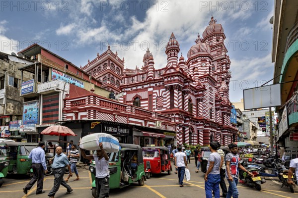 Bustling street scene with rickshaws and passers-by in front of a red architectural building, the old town with the red mosque in Colombo Sri Lanka