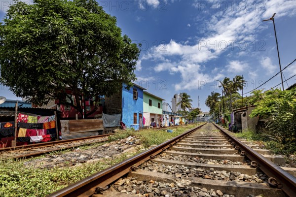 Railway tracks run along colorful houses and a large tree under a cloudy sky, railway line in the historic Slave Island district in Colombo Sri Lanka