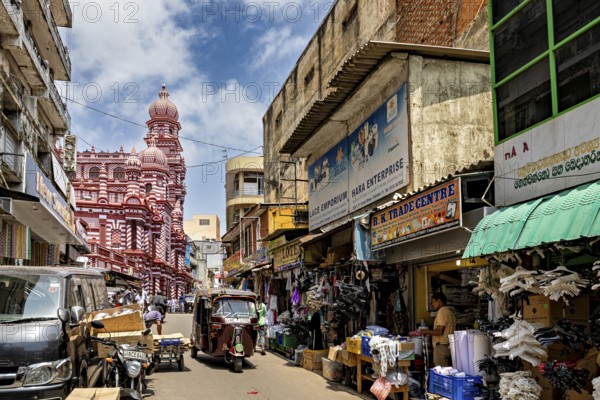 Bustling market street with people and stalls, red architectural building in the background, the old town with the red mosque in Colombo Sri Lanka
