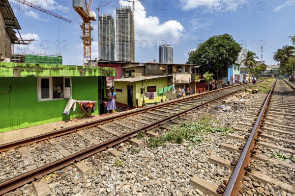 Railway tracks next to colorful houses with skyscrapers in the background and construction crane under a blue sky, railway line in the historic Slave Island district in Colombo Sri Lanka