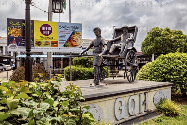 Sculpture of a person drawing a rickshaw surrounded by green bushes and advertising in the background, monument of a rickshaw in the streets of Colombo Sri Lanka
