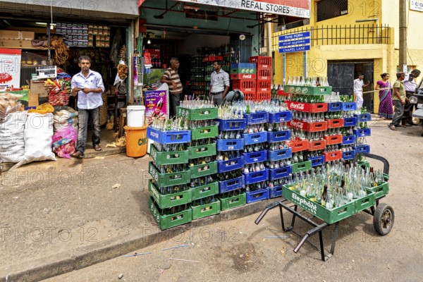 A small shop with boxes full of bottles in front of the entrance, surrounded by busy street activity, beverage shop in the streets of Slave Island in Colombo Sri Lanka
