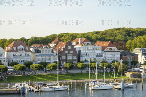 Picturesque houses and boats stand on a sunny harbor against a green forest backdrop, Lübeck-Travemünde, Schleswig-Holstein, Germany