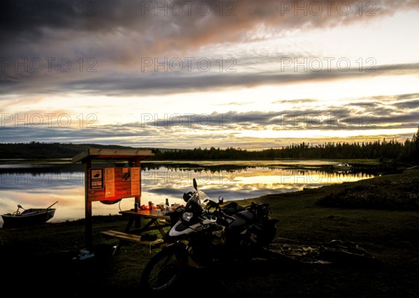 A BMW model G 650 GS Sertao motorcycle stands in front of a lake at sunset with dramatic clouds in the sky and reflecting water surfaces Dorotea, Västerbottens län, Sweden