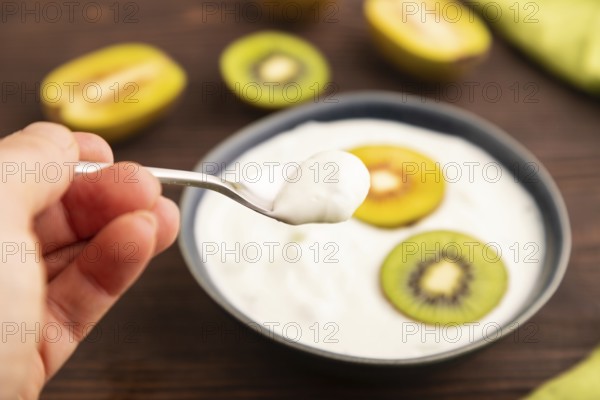 Yogurt, with kiwi in blue bowl on brown wooden background and green linen textile with hand, side view, close up, minimalism, selective focus