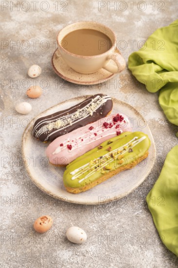 Glazed Eclairs on brown concrete background and green linen textile, cup of coffee, side view, close up