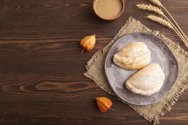Glazed Pies with Cowberry jam on brown wooden background and linen textile, cup of coffee, top view, flat lay, copy space