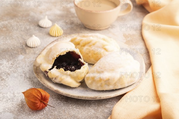 Glazed Pies with blueberry jam on brown concrete background and orange linen textile, cup of coffee, side view, close up