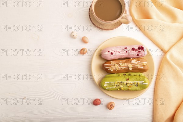 Glazed Eclairs on white wooden background and orange linen textile, cup of coffee, top view, flat lay, copy space