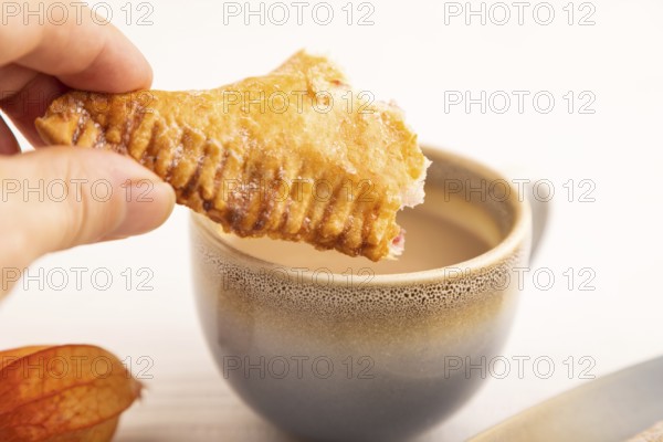 Triangles Pie, Puff Pastry, Samsa with cherry jam with hand on white wooden background, cup of coffee, side view, close up, selective focus