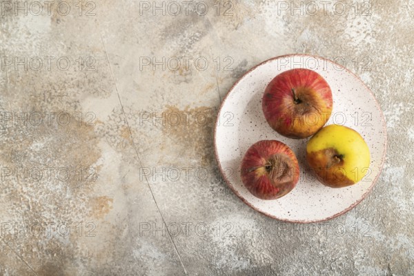 Decaying, Rotting apples on ceramic plate on brown concrete background. Top view, copy space, flat lay, minimalism