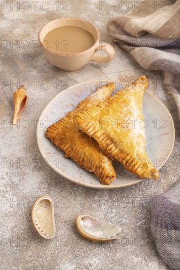 Triangles Pie, Puff Pastry, Samsa with cherry jam on brown concrete background and linen textile, cup of coffee, side view, close up