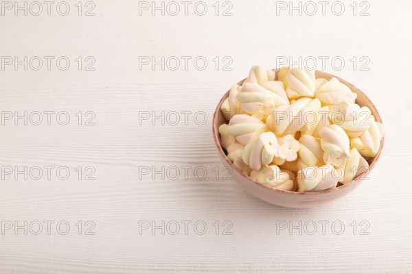 Orange and pink marshmallow in ceramic bowl on white wooden background, side view, copy space, minimalism
